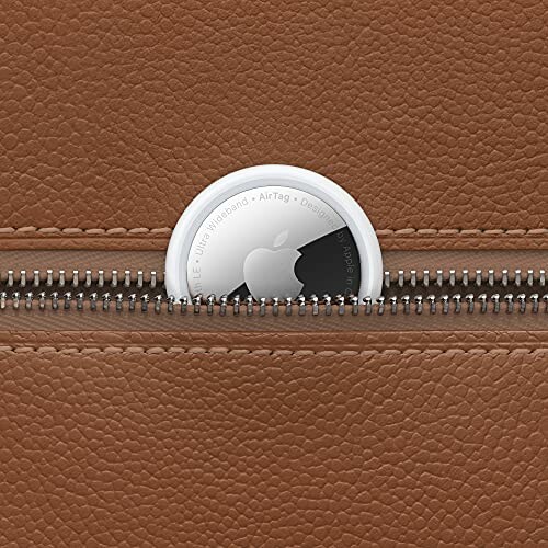 Apple AirTag partially inserted in a brown leather bag's zipper.