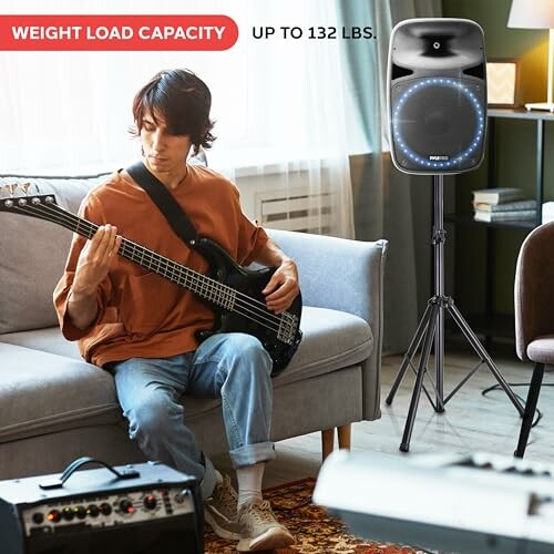 Man playing electric guitar with speaker on stand nearby in living room.