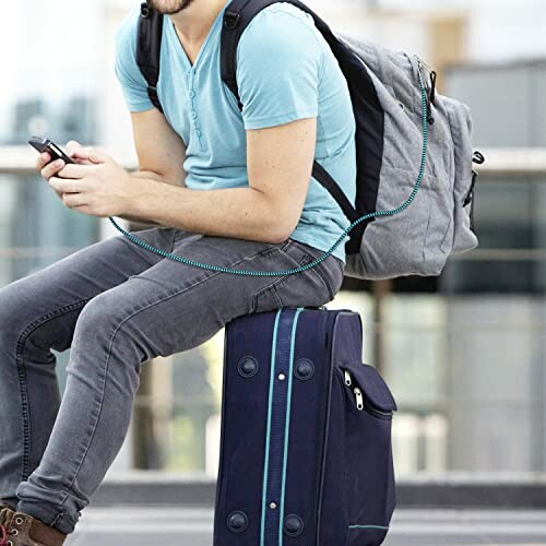 Man sitting on luggage with backpack and phone.