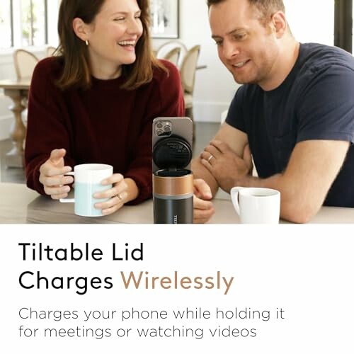 Two people using a tiltable lid wireless phone charger with mugs on a table.